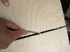 A person cutting a slit in a piece of plywood.