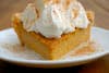 An orange slice of sweet-potato pie with whipped cream on top and a dusting of orange spice, possibly nutmeg.