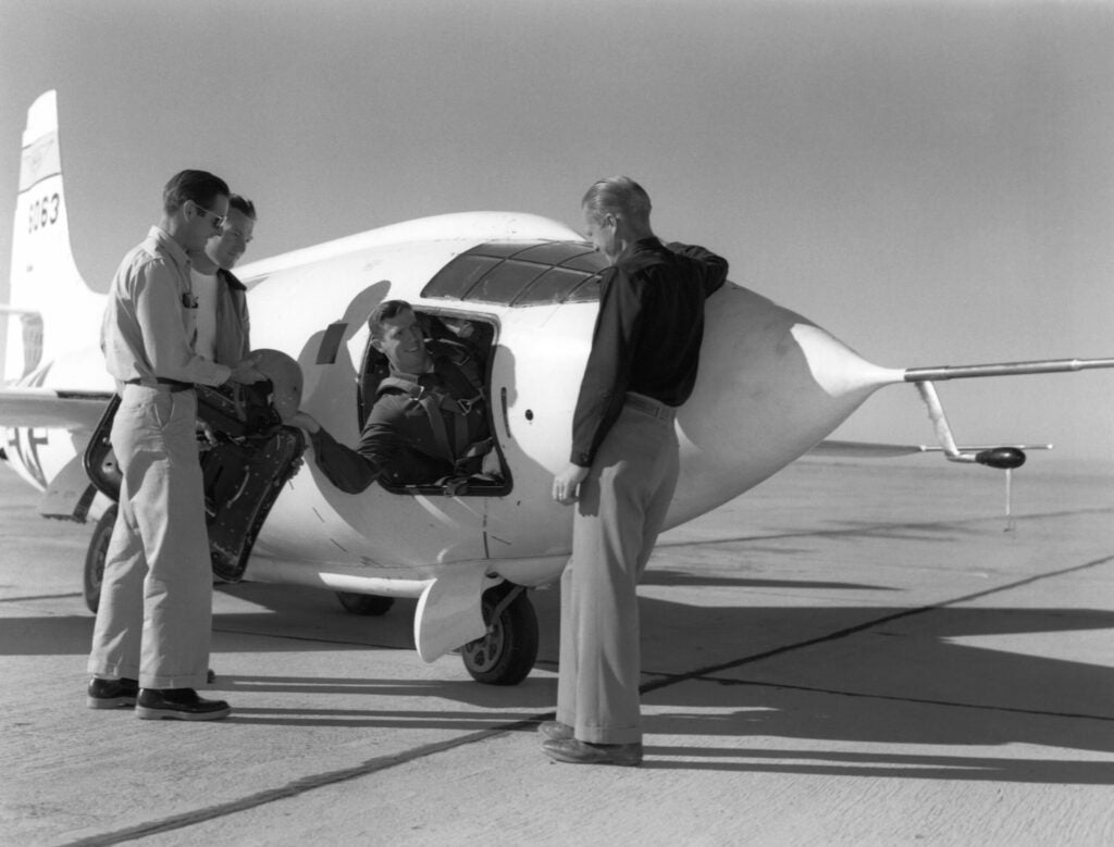 John Griffith hands off his flight gear to ground crew members, hanging out the hatch of an X-1.