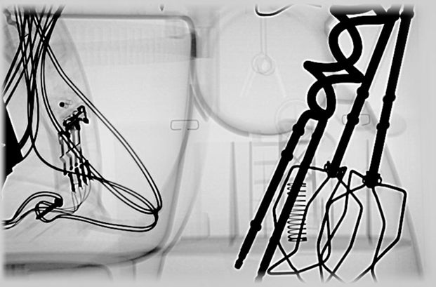In this backscatter x-ray, the darker parts reveal the dense metal and wire components of a hand mixer.