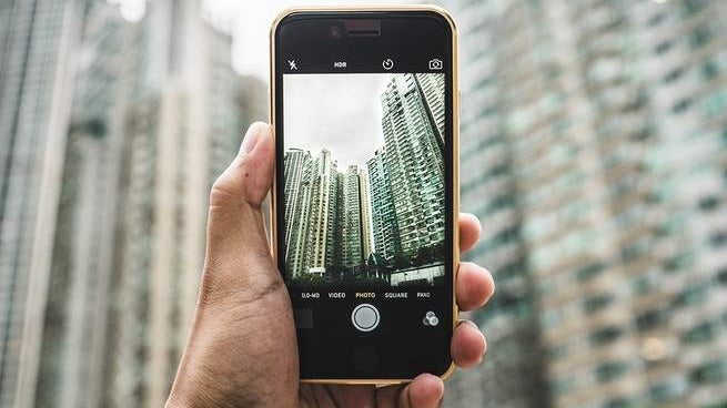 A person holding an iPhone and looking through the camera app at some tall buildings.