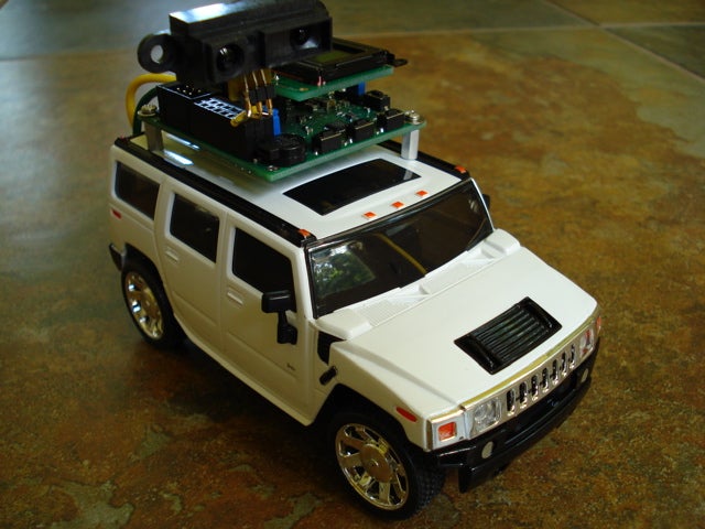 A white remote-controlled truck with an Arduino on top of it, on a concrete floor.