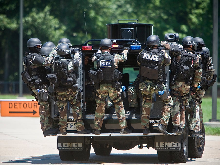 Virginia Beach SWAT team members ride the running boards of an armored van to get into position to assault Building 1155.