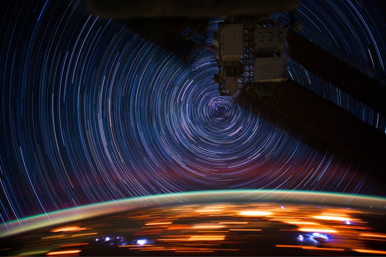 A time lapse photograph of stars and the lights of earth below.