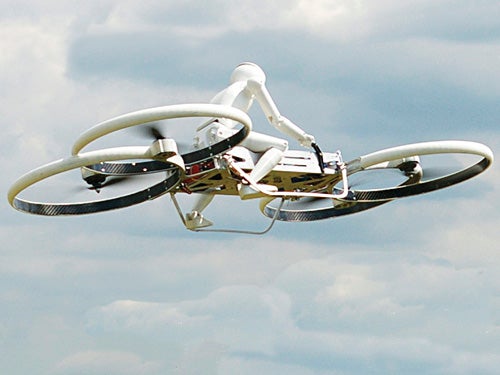 A small figure on a flying prototype quadcopter, both in white, on a cloudy blue-gray sky