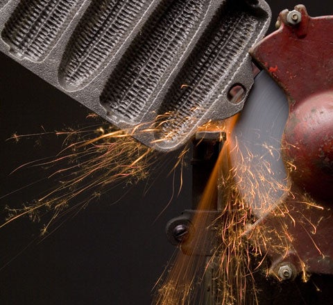 A person holding cast iron against a grinder, producing orange sparks.