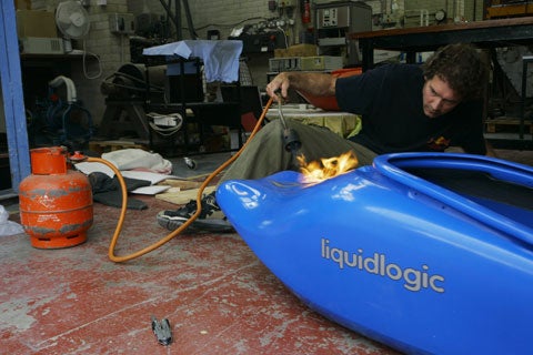 Shaun Baker uses fire to modify his blue kayak in a garage.