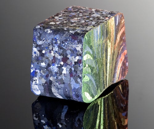 A piece of pure aluminum after being treated with muriatic acid, having changed color to blue, green, yellow, and red, with crystal-like patterns.