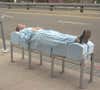 A woman lies on a bench designed to deter lying down by wearing an special suit designed by artist Sarah Brown