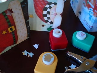 Holiday cards, a star-shaped hole punch, and some other crafting tools on a black surface.