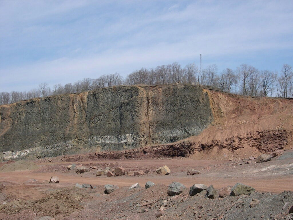 In Clifton, New Jersey, a massive basalt flow (black rock on left) from the time of the End Triassic is exposed in a former quarry, now located behind a retirement home. Reddish sedimentary rocks signaling the extinction itself lie to the far right.