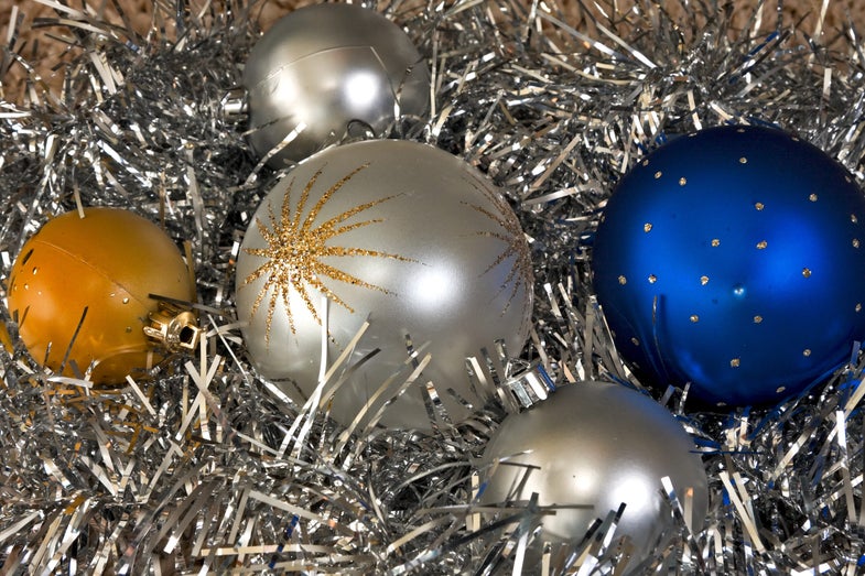 Five different round baubles used as ornaments to decorate the Christmas tree. All of them are standing on several strips of shiny tinsel. The gray one in the center has a golden sparkling star with long rays. Next to it there is a deep blue one with yellow dots replicating the midnight sky.