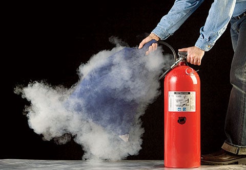 A person spraying a fire extinguisher into a pillowcase against a black background.