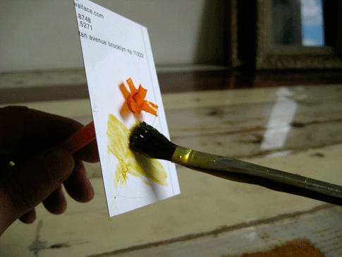 A person using a brush to spread rubber cement on a piece of paper that has a straw sticking through it.