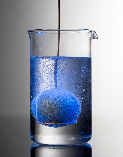 A ball of zinc being dipped into a beaker containing muriatic acid. Bubbles are coming off the zinc.