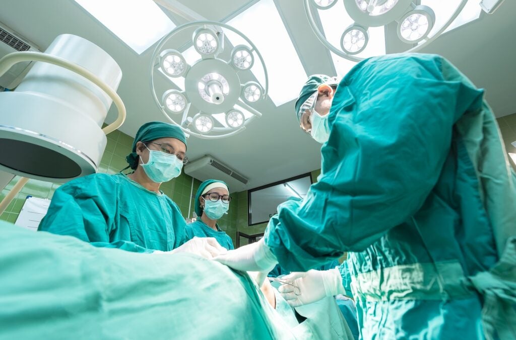 Three doctors in green surgical scrubs operating on a patient in the emergency room.