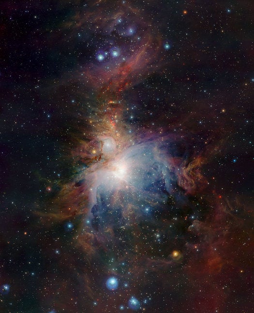 In this image of the Orion nebula, the VISTA telescope turned its infrared vision upon the young stars emerging in and around the visible cloud of gas enshrouding the stellar nursery. A red region directly above the center of the image reveals young stars that continue to form amidst clouds of interstellar gas. Such stars can eject gas at speeds of almost 435,000 miles per hour (700,000 km/hr).