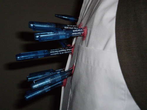 A man's chest in a white buttondown shirt with several blue pens stuck in it as part of a Halloween costume mimicking stab wounds.
