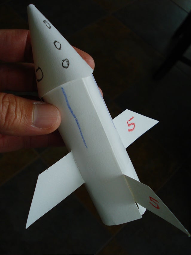 A small paper rocket in a person's hand against a black background.