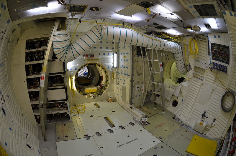 Atlantis' middeck, as viewed from the opposite perspective as the earlier photo. Here, the crew access hatchway is seen to right, and the airlock hatchway is center. The waste collection system (toilet) compartment, now empty, is behind the ladder to the right.