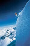 Skier in a yellow jacket skiing off of a snow cliff