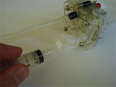 A person using a syringe to drain water out of a clear plastic tube.