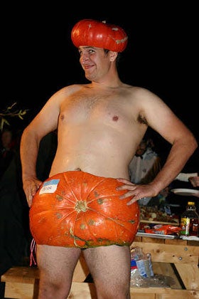 A man wearing only a pumpkin for a hat and a pumpkin around his waist.