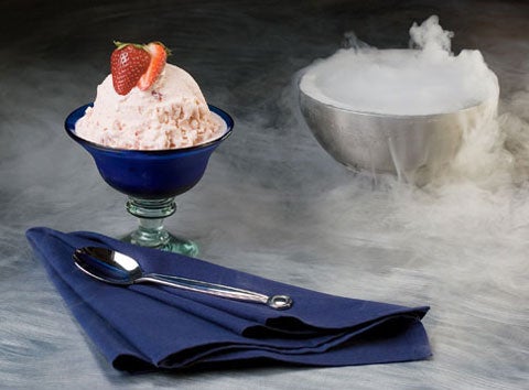 Ice cream made with a fire extinguisher in a goblet next to a napkin and a spoon, with dry ice vapor all around.