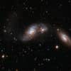 IC 4687 forms a triplet with two other galaxies: IC 4686 to the right and IC 4689 further to the right. IC 4687 has a chaotic body of stars, gas and dust and a large curly tail to the left. The two companions are partially obscured by dark bands of dust. The interacting triplet is about 250 million light-years away from Earth, in the constellation of Pavo, the Peacock.