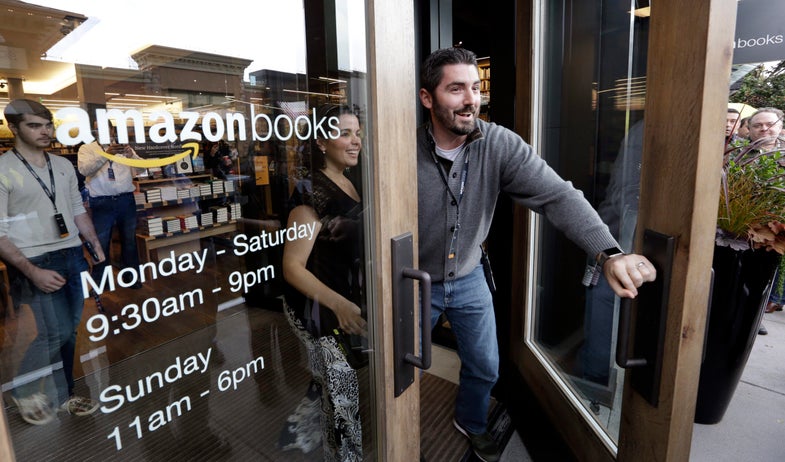 Employees smile as they unlock and open the door to the first customers at the opening day for Amazon Books, the first brick-and-mortar retail store for online retail giant Amazon, Tuesday, Nov. 3, 2015, in Seattle. The company says the Seattle store, coming two decades after it began selling books over the Internet, will be a physical extension of its website, combining the benefits of online and traditional book shopping. Prices at the store will be the same as books sold online. (AP Photo/Elaine Thompson)