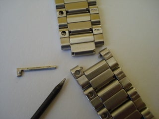 A silver watch band with a link pin removed.