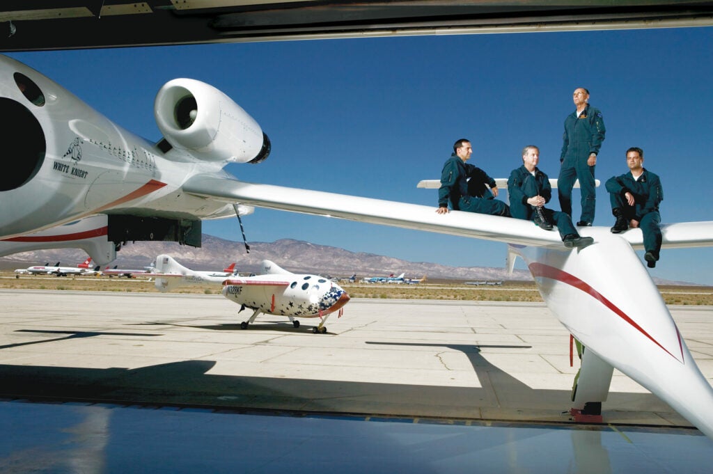 From left, Brian Binnie, Doug Shane, Mike Melvill, and Peter Siebold on <em>White Knight.</em> In the background, <em>SpaceShipOne</em> awaits its final two flights.