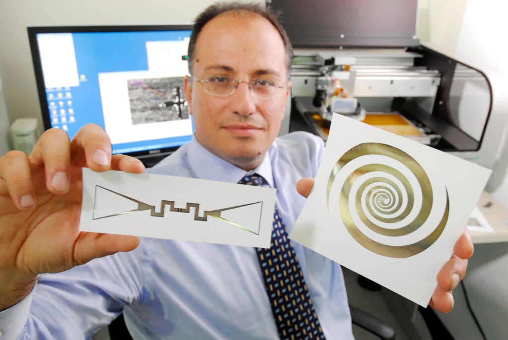 Tentzeris holds a sensor (left) and an ultra-broadband spiral antenna for wearable energy-scavenging applications. Both were printed on paper using inkjet technology.