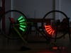 A bicycle upside-down in the dark, using persistance-of-vision circuit boards to display green words on one wheel and red words on the other.