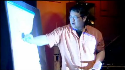 Johnny Chung Lee points at a large screen.