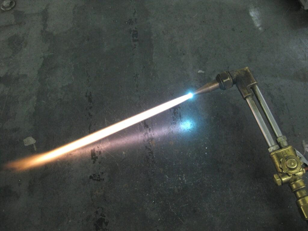 An oxy-acetylene cutting torch on a concrete floor with its flame on.