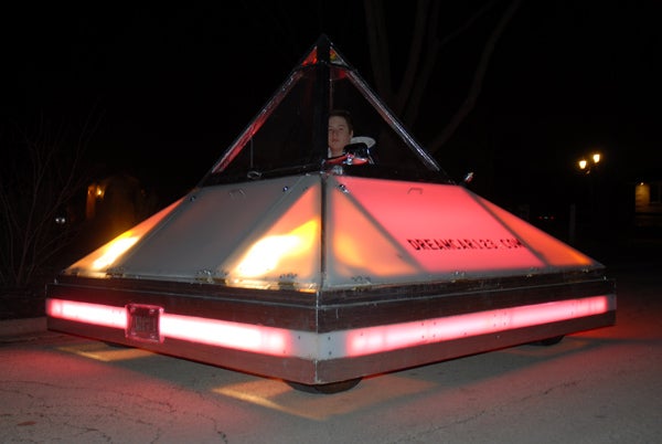 A pyramid-shaped car with lights around it, at night.