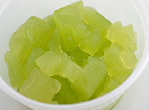 Frozen cubes of broken honeydew melon in a white bowl.