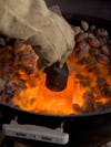 A person wearing thick heat-proof gloves stamping a pattern in molten glass over a fire.