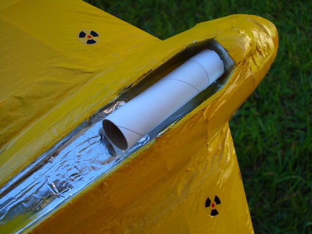 A yellow model plane with aluminum foil lining an area where a model rocket will sit in the fuselage.