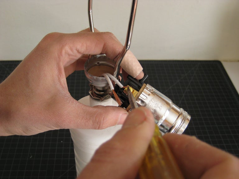 A person adding a light bulb socket to a plastic homemade lamp.