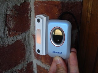 A person pressing a doorbell on a brick wall near a door.