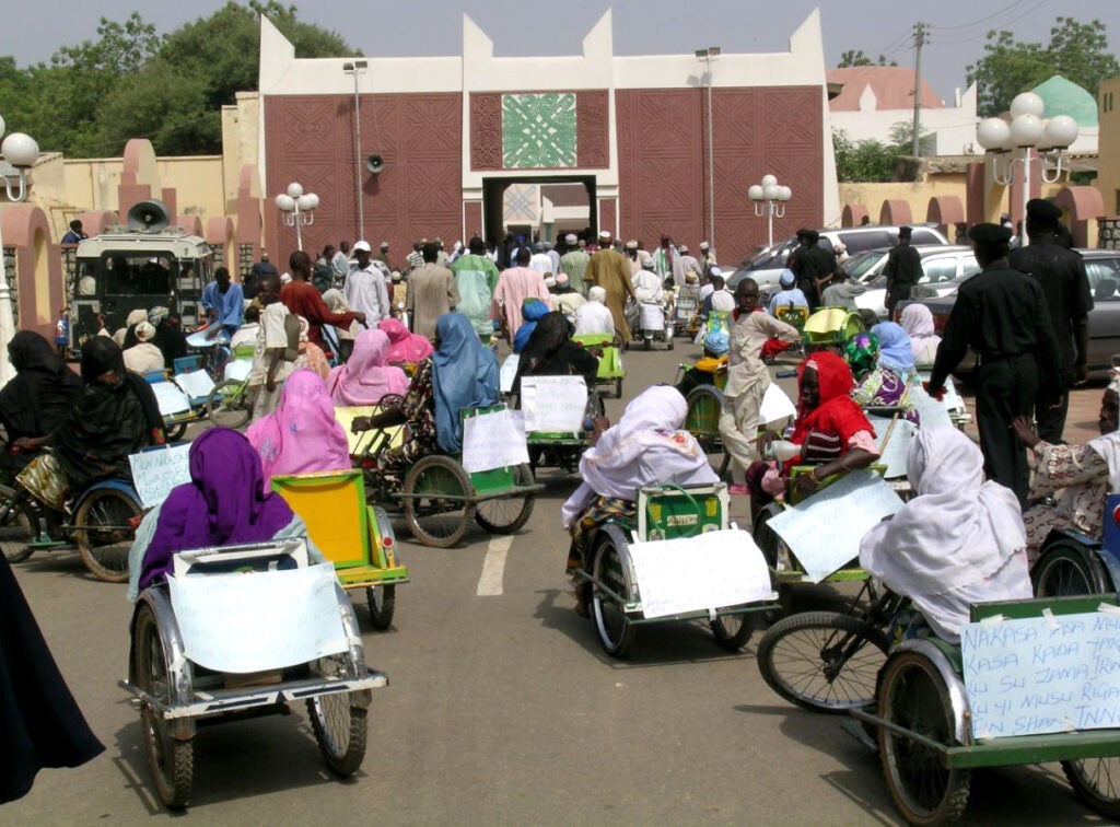 photo of women polio survivors on tricycles in front of a palace in northern Nigeria