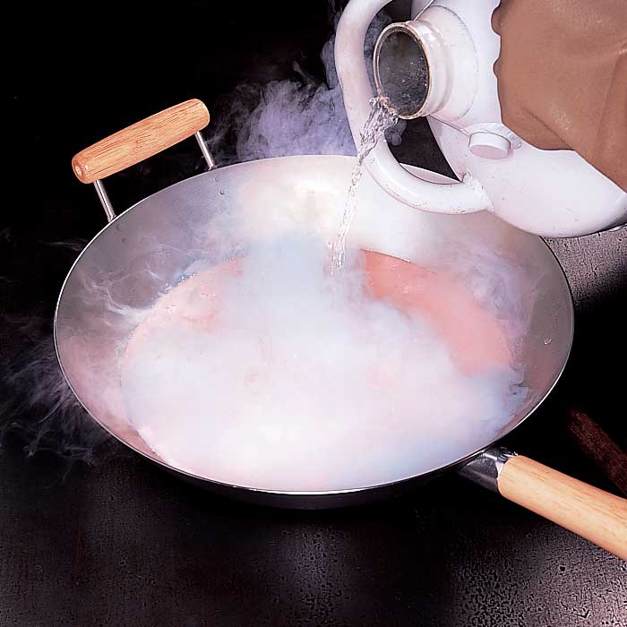 A person pouring liquid nitrogen from a tank into a metal wok.