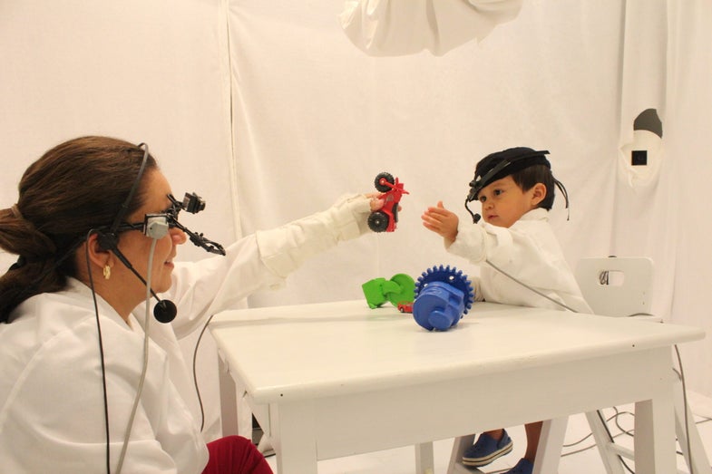 Wearing head-mounted eye-tracking technology, a child and his mother engage in free play with objects for researchers to observe the dynamics of their social interaction.