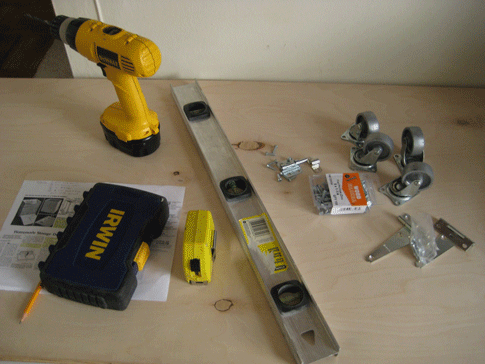 A power drill, a level, other tools, and a sheet of plywood.