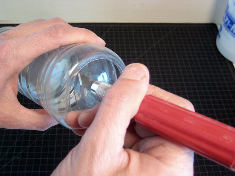 A person using a sharp knife to cut the bottom off of a plastic bottle.