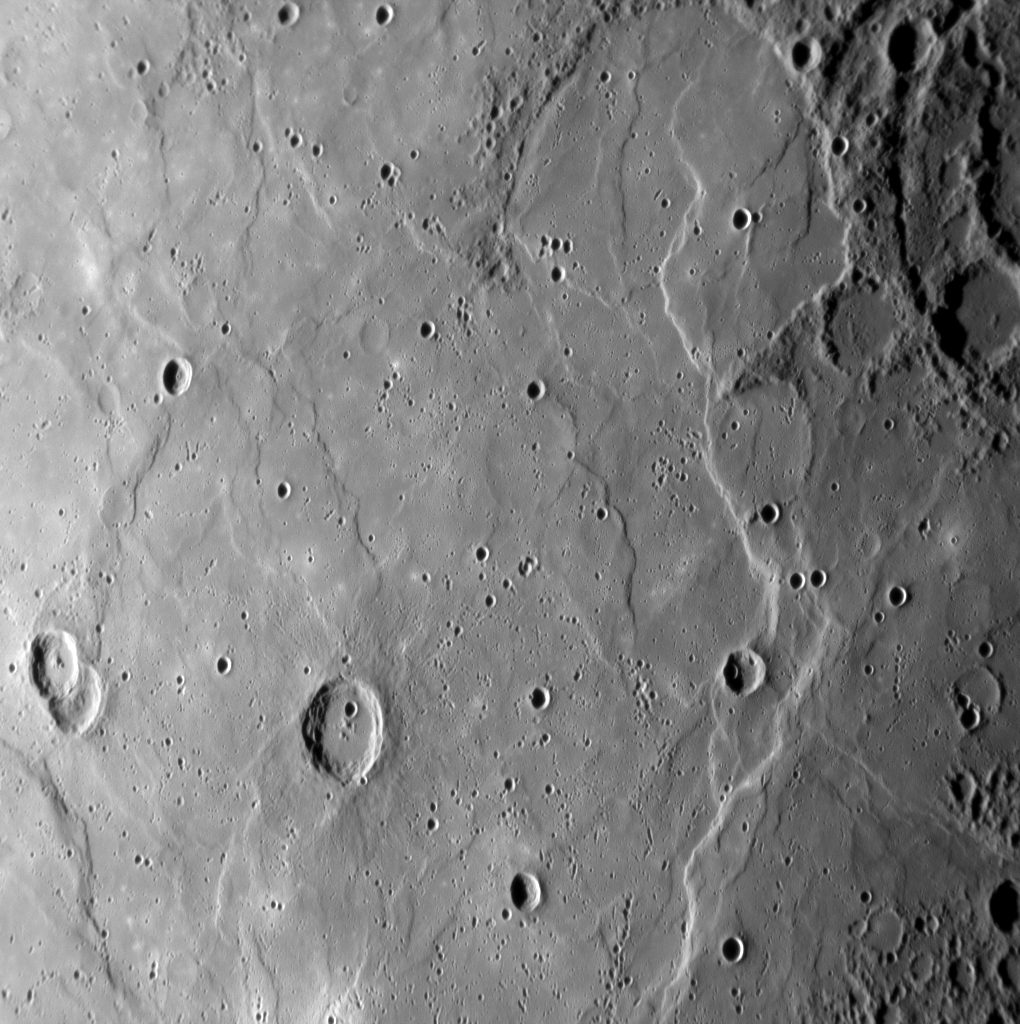 This image shows a large expanse of smooth plains material. The density of impact craters on the smooth plains is less than on the heavily cratered terrain visible in the upper right and lower right corners of the image. The presence of fewer impact craters means that the plains are young compared with the older, battered terrain. Despite their relative youth, tectonic forces in Mercury's crust have produced the curving scarps (cliffs) and "wrinkle ridges" that run mostly from top to bottom in the image.