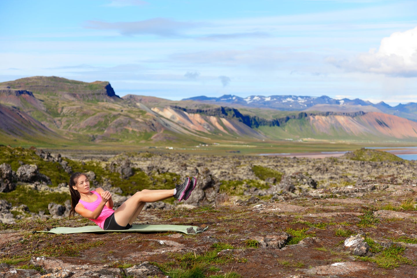 Fitness woman doing russian twist core exercise outside. Fit female training stomach in amazing nature landscape on Iceland. Fit female sport model girl training crossfit outdoors. Mixed race athlete.