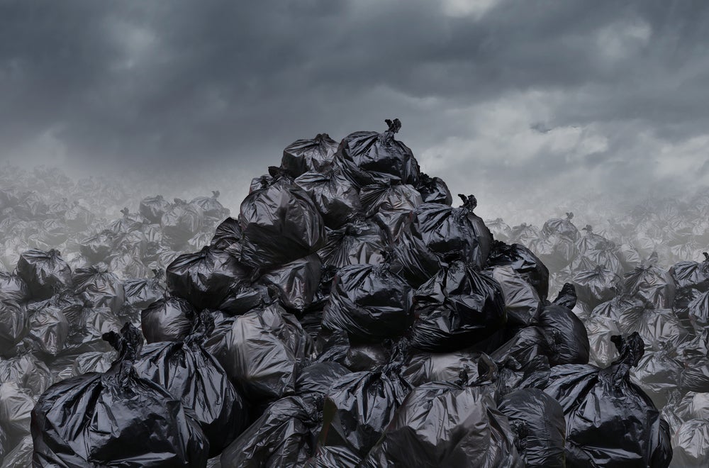 Garage dump concept with mountains of black waste bags of trash with an unpleasant smell in an infinite landfill heap landscape as a background of environmental damage issues on a foggy dark cloudy scene.